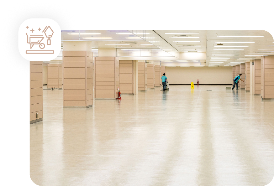 Two professional cleaners in a large, empty commercial space, using floor polishing machines for a post-construction cleanup.